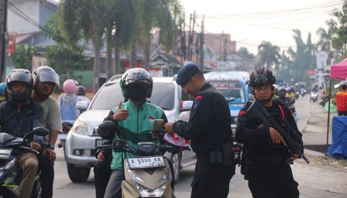 Personel Brimob Polda Banten membagikan dan memasang bendera Merah Putih kepada pengendara motor dalam rangka menyambut HUT ke-80 RI. (Foto: Bantentv.com)