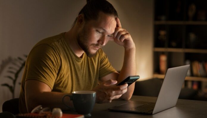 Seorang pria terlihat fokus menatap layar HP di malam hari kebiasaan doomscrolling seperti ini sering membuat banyak orang sulit beristirahat dan merasa lelah tanpa sadar.