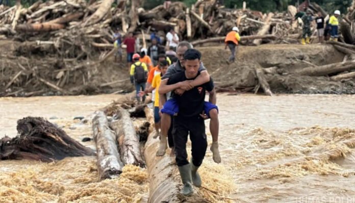 Anggota Brimob Polri mengevakuasi korban dengan melintasi batang kayu di tengah derasnya arus banjir bandang.